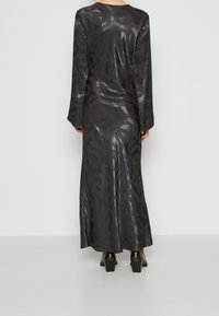 Lång svart klänning med en slät, glänsande yta och ett virvlande texturmönster. Har lång ärm och en rak silhuett som når anklarna.