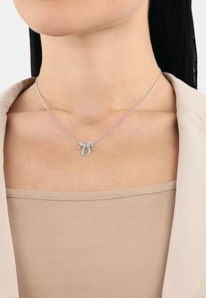 Collana d'argento con design a loop decorativo, impreziosita da piccole pietre trasparenti, posata sulla clavicola di un modello.