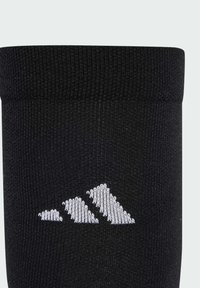 Crna čarapa s teksturiranim tkanjem i preklopnim vrhom. Sadrži bijeli izvezeni logo tri oblikovane planine sa strane.