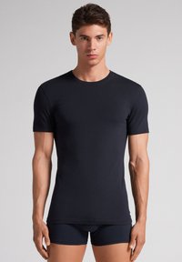 Marineblaue Kurzarm-T-Shirt aus glattem Stoff, mit Rundhalsausschnitt und enganliegendem Design, kombiniert mit dunklen Shorts.