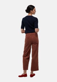 Un pull à manches courtes en maille côtelée navy associé à un pantalon large en velours côtelé rouille et des chaussures plates rouges, vue de dos. Texture et détails visibles.