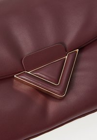 Bordeaux leren clutch met een gestructureerde afwerking. Bevat een gouden driehoekige hardware-accent op de klep. Strak, minimalistisch ontwerp.