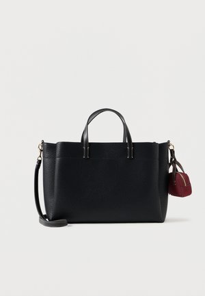Tote bag en cuir noir avec deux poignées, une bandoulière détachable et une petite pochette rouge attachée sur le côté. Surface texturée.