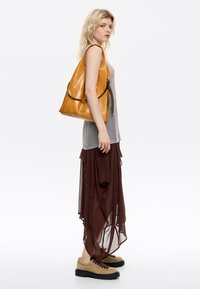 Bolso hobo de cuero amarillo con ribete negro, falda corta de capas en tono marrón, blusa de punto gris y zapatos beige con cordones y suelas gruesas.