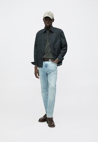 Dark plaid shirt, gray T-shirt, light blue jeans, brown leather shoes, and beige cap. The look features a casual fit with textured fabrics.