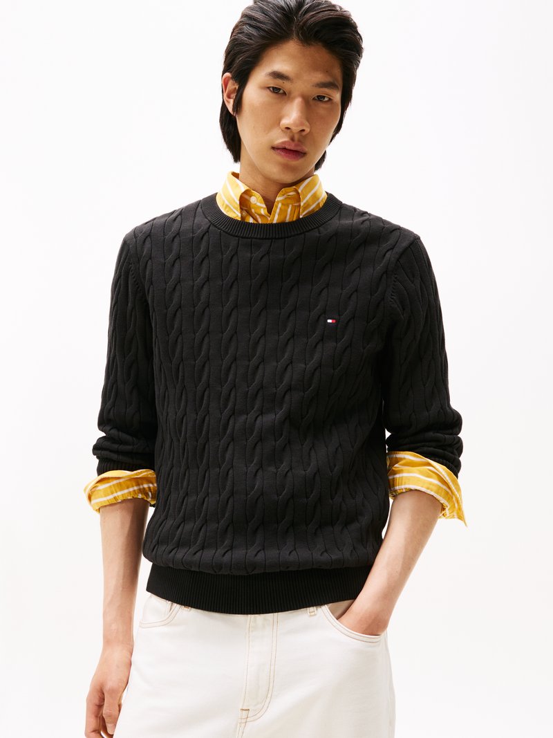 Μαύρο πουλόβερ με στρώσεις καλωδίων και ριγέ λαιμόκοψη και στρίφωμα, που είναι φορεμένο πάνω από ένα κίτρινο και άσπρο ριγέ πουκάμισο με γιακά. Άσπρο παντελόνι, casual εφαρμογή.