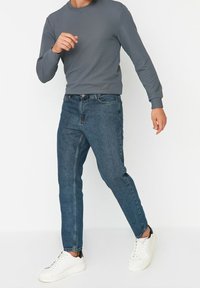 Camisa de manga larga gris con textura acanalada, combinada con jeans de mezclilla azul. Los zapatos son blancos con detalles negros. Diseño minimalista y casual.