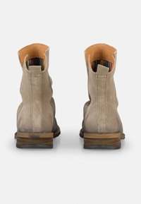 Botines de ante beige con una textura ligeramente desgastada, tacón apilado marrón y forro de cuero naranja. Presenta un diseño interior a rayas.