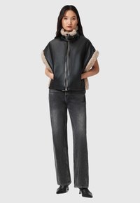 Juoda odinė liemenė su smėlio spalvos dirbtinio avikailio apdaila, užtrauktuku užsegama ir ryškios, laisvos formos siluetu, derinama su juodais aukšto liemens džinsais ir aulinukais.