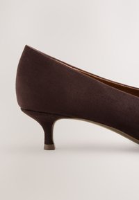 Escarpin femme en suède marron à talon bas, avec un bout arrondi et un petit talon kitten sur un fond clair uni.
