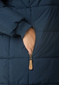 Navy pufferjack met een gequilte design. Beschikt over geribde manchetten en een ritszak met een leren trekker in tan. Glad textuur.