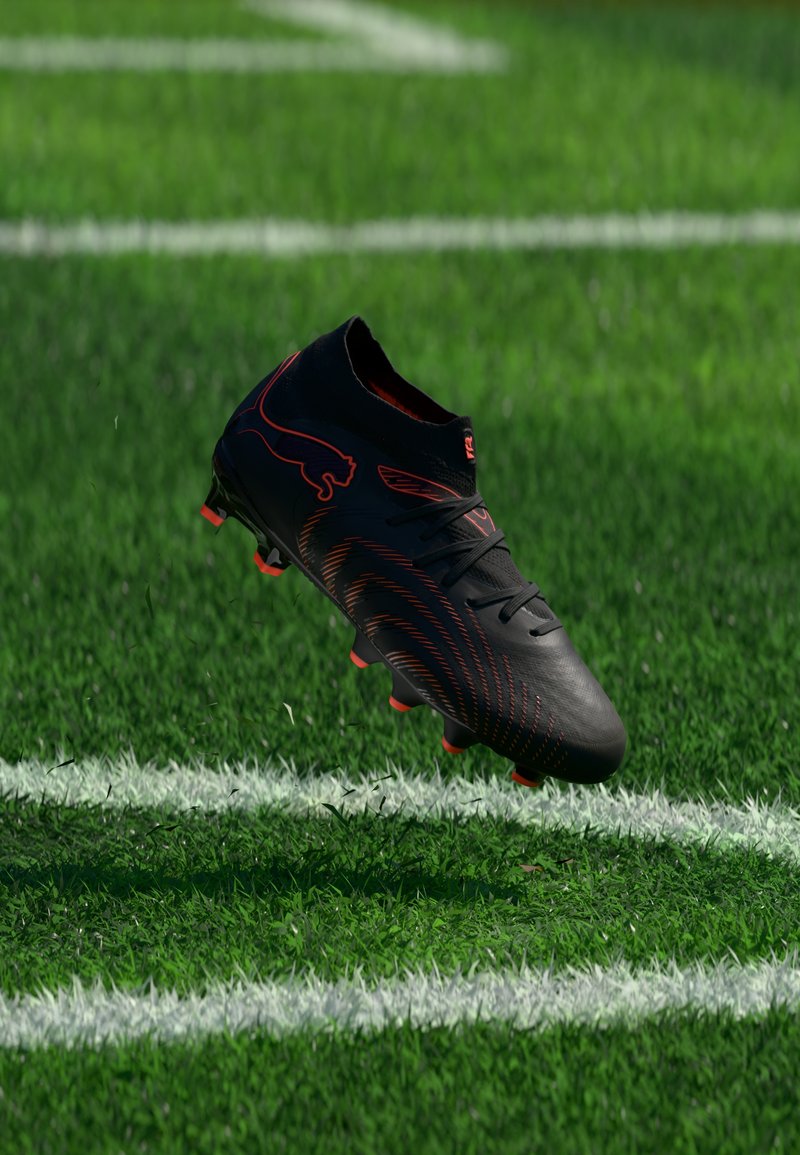 Μαύρο και κόκκινο παπούτσι ποδοσφαίρου να αιωρείται πάνω από λευκές γραμμές αγωνιστικού χώρου σε πράσινο χορτάρι, εμφανιζόμενο από πλάγια γωνία με ορατό λογότυπο της μάρκας.