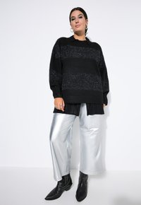 Maglione nero a righe con lavorazione a maglia, indossato sopra una camicia a righe sottili. Pantaloni argentati a gamba larga e stivaletti neri con dettagli borchiati.