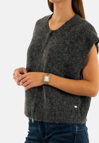 Maglione senza maniche in lana grigia con finitura testurizzata, scollatura rotonda e dettaglio in zip metallica sull'orlo. Indossato con jeans blu.