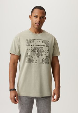 Jasnozielona bawełniana koszulka z okrągłym dekoltem, zdobiona czarnym wzorem paisley i słowem "diverse" na środku. Krótkie rękawy.