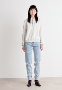Moletom cinza claro com zíper de meia, combinado com jeans claros desfiados. Usado com botas pretas até o tornozelo. Design simples e casual.