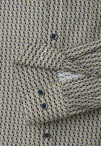 Button-up shirt featuring a geometric pattern with navy, cream, and mustard colors; cotton fabric; black buttons; adjustable cuffs.