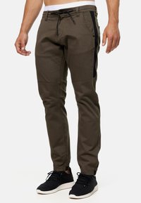 Olivengroene taps toelopende broek met zwarte zijpanelen, elastische tailleband, trekkoordsluiting en subtiele gestructureerde stof. Ideaal voor casual gebruik.