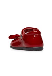 Zapato plano de charol rojo con punta redonda, parte trasera redondeada y un detalle decorativo de lazo en la parte delantera. Presenta una suela negra flexible.