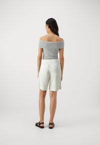 Gray off-the-shoulder ribbed top paired with knee-length cream shorts featuring a subtle circular pattern and black sandals.