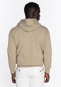 Sudadera beige con capucha, textura acanalada y mangas largas, con un ajuste holgado. Pantalones blancos con dos bolsillos traseros y detalle de botones.