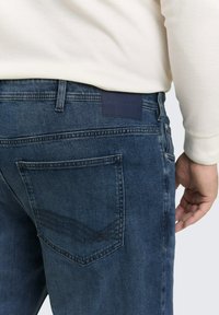 Dunkelblaue Jeans aus Denim mit einer strukturierten Oberfläche, mit einem Patch am Bund und einzigartigen Nähten auf den hinteren Taschen.