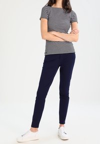 Haut à manches courtes rayé en bleu marine et blanc ; associé à un pantalon bleu marine. Le modèle porte des baskets blanches. Design simple et ajusté.