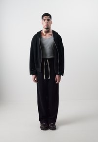 Black zip-up hoodie over a gray tank top, paired with loose black sweatpants and chunky black sneakers. Simple design, soft textures.