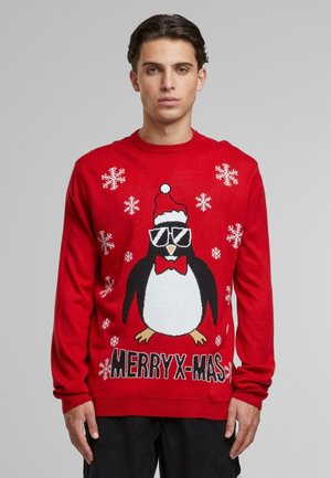 Pull rouge avec un motif de pingouin portant des lunettes de soleil, un chapeau de Noël et un nœud papillon, avec des flocons de neige et le texte "JOYEUX NOËL".