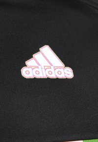 Tessuto nero con superficie testurizzata caratterizzato da un logo Adidas bianco contornato da accenti rosa e gialli, posizionato diagonalmente.