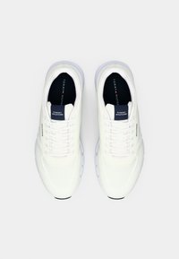 Pair of white Tommy Hilfiger knit sneakers with laces, black insoles featuring Tommy Hilfiger logo, viewed from above on a white background.