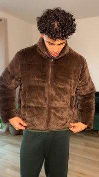 Braune Fleecejacke mit Reißverschluss und hohem Kragen, mit weicher Textur und gesteppte Einsätze, getragen über dunkelgrünen Hosen.