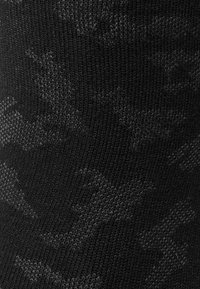 Tejido de punto negro con un sutil patrón de camuflaje, que presenta diferentes tonos de gris para dar textura y profundidad. Detalle en primer plano del diseño textil.
