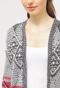 Svart och vit mönstrad cardigan med öppen front, som har en texturerad stickdesign och rosa detaljer vid nederkanten. Även lös passform.