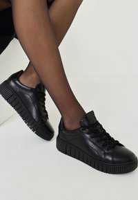 Svarta lädersneakers med tjocka gummisulor, texturerade detaljer och rund tå. Snören och vadderad tunga ger komfort. Accenter i matt finish.