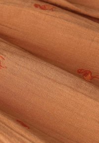 Tissu en coton de couleur terracotta chaude avec une surface douce et texturée, arborant une broderie rouge subtile de motifs complexes.