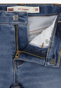 Jean Levi's 514 droit, en denim, couleur bleue, avec une fermeture éclair en laiton, un bouton de fermeture et des détails de couture beige. Étiquette de taille visible.