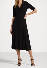 Svart, knälång klänning med korta ärmar och en krage. Har en knäpptstängning och en utsvängd nederdel. Slät textur.