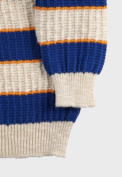 Manche et ourlet de pull en maille épaisse couleur crème avec des rayures horizontales bleues et fines orange, texture côtelée.
