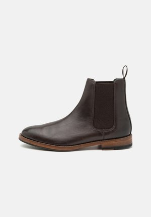 Dark brown leather Chelsea boot with elastic side panel, pull loop at the back, and wooden sole with a small heel on a white background.