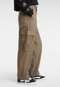 Cargo broek gemaakt van lichtbruine stof, met zijzakken, gestikte details en een relaxte pasvorm, gecombineerd met zwarte sneakers.