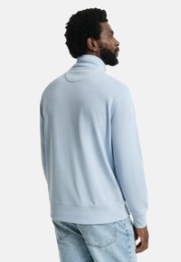 Helles blaues Fleece-Sweatshirt mit hohem Kragen und langen Ärmeln. Verfügt über einen gerippten Saum und Bündchen, eine glatte Textur und eine lockere Passform.