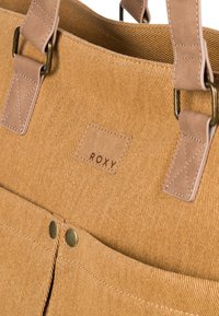 Sac en toile de velours côtelé marron avec des accents en cuir beige, équipé d'une étiquette 'ROXY', de deux boutons en laiton et d'une finition texturée.