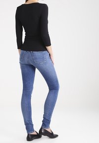 Černý přiléhavý top s třičtvrtinovými rukávy doplněný modrými slim-fit džíny. Celkový outfit doplňují černé ploché boty.