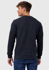 Navy textured sweatshirt with a round neckline, ribbed cuffs and hem, and a slim fit, paired with blue jeans.