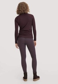 Mouwloze, donker bordeaux top met een aansluitend ontwerp en gathered achterkant. Gecombineerd met gestructureerde, donkerpaarse leggings en bruine enklaarsjes.