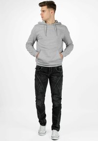 Grijze hoodie met een buidelzak, gecombineerd met zwarte jeans met witte stiksels. Model draagt witte sneakers.