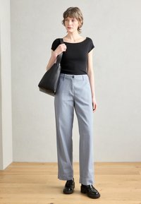 Black, fitted short-sleeve top; light blue, high-waisted, wide-leg pants; black, structured handbag; shiny black shoes; wooden floor background.