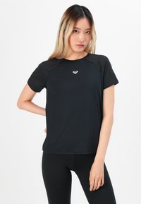 Svart t-skjorte med kort erm og rund hals, med raglanermer og en liten hvit logo plassert midt på brystet. Mykt og glatt stoff.