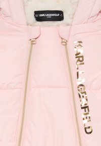 Casaco acolchoado rosa claro com interior peludo, apresentando fechos metálicos dourados e o texto "KARL LAGERFELD" em dourado na frente.